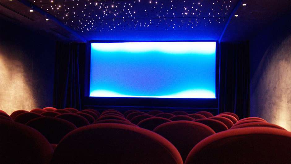 Ein leerer Kinosaal samt Sternenhimmel, rote Stühle, blau schimmernder Screen