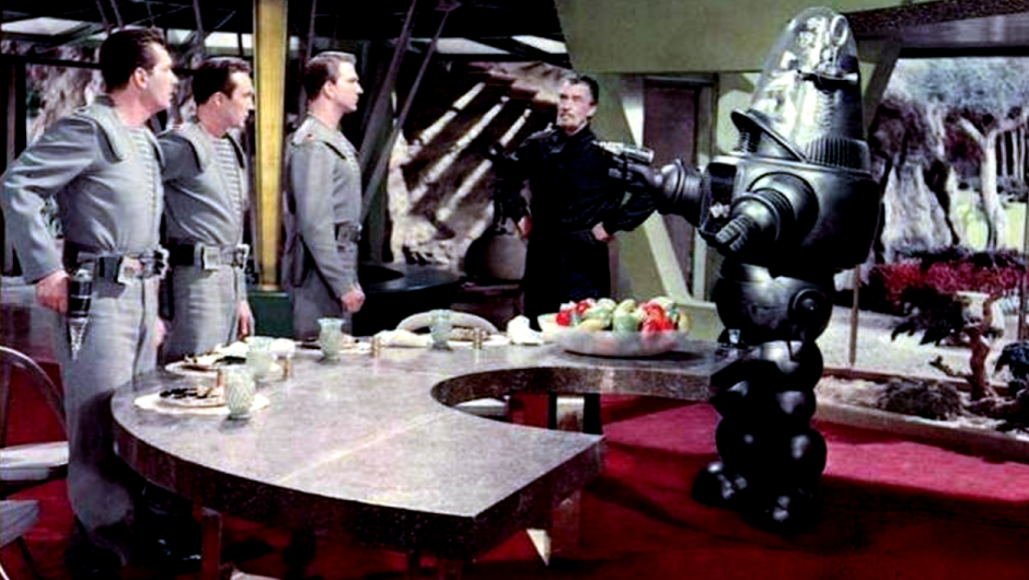 Drei Männer in Raumanzügen, ein älterer in schwarzer Kleidung und ein Roboter, der eine Laserkanone hält