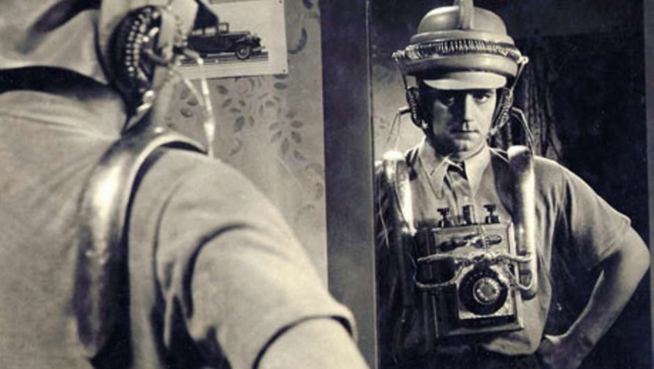 Ein Mann sieht sein Spiegelbild, dabei trägt er eine vertrackte Apparatur am Körper