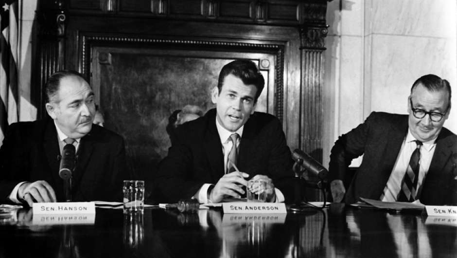 Drei Männer sitzen an einem runden Tisch, man sieht nur die Oberkörper, schwarz-weiß Fotografie