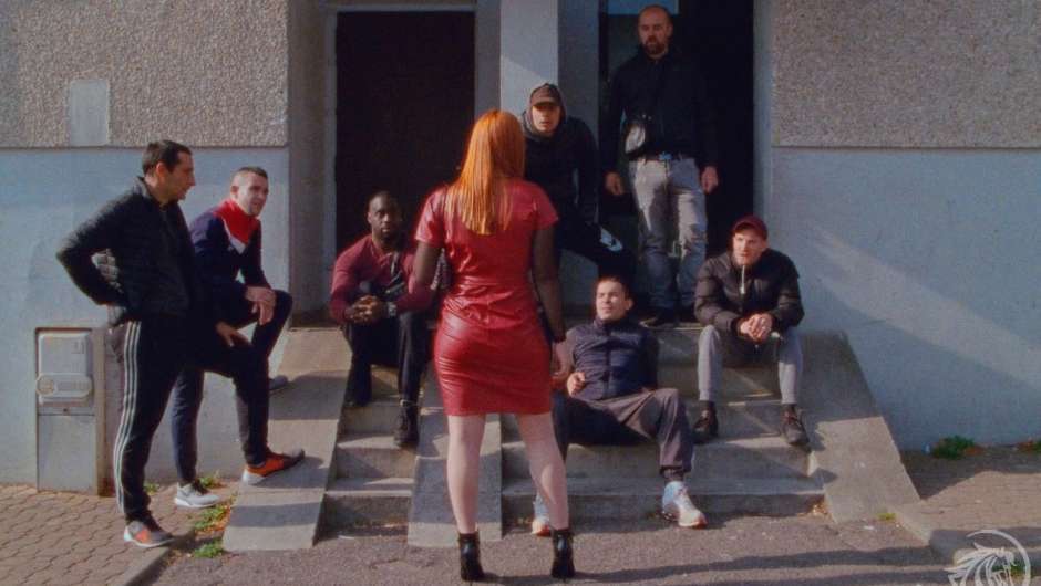 viele Männer, die auf einer niedrigen Treppe herumlungern, davor eine Frau in rotem Kleid mit dem Rücken zu den Betrachter*innen