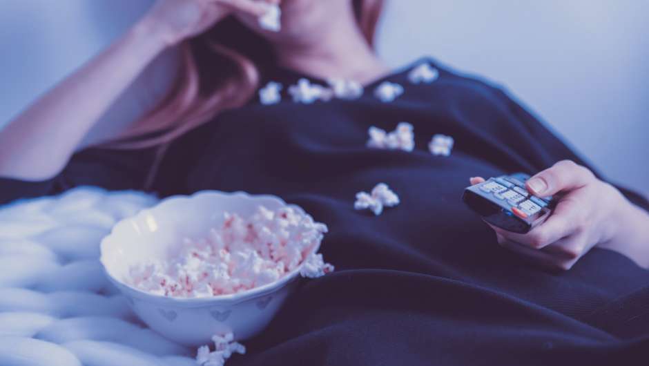 Frau auf Couch mit Popcorn und Fernbedienung 