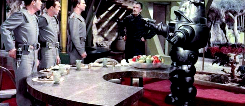 Drei Männer in Raumanzügen, ein älterer in schwarzer Kleidung und ein Roboter, der eine Laserkanone hält